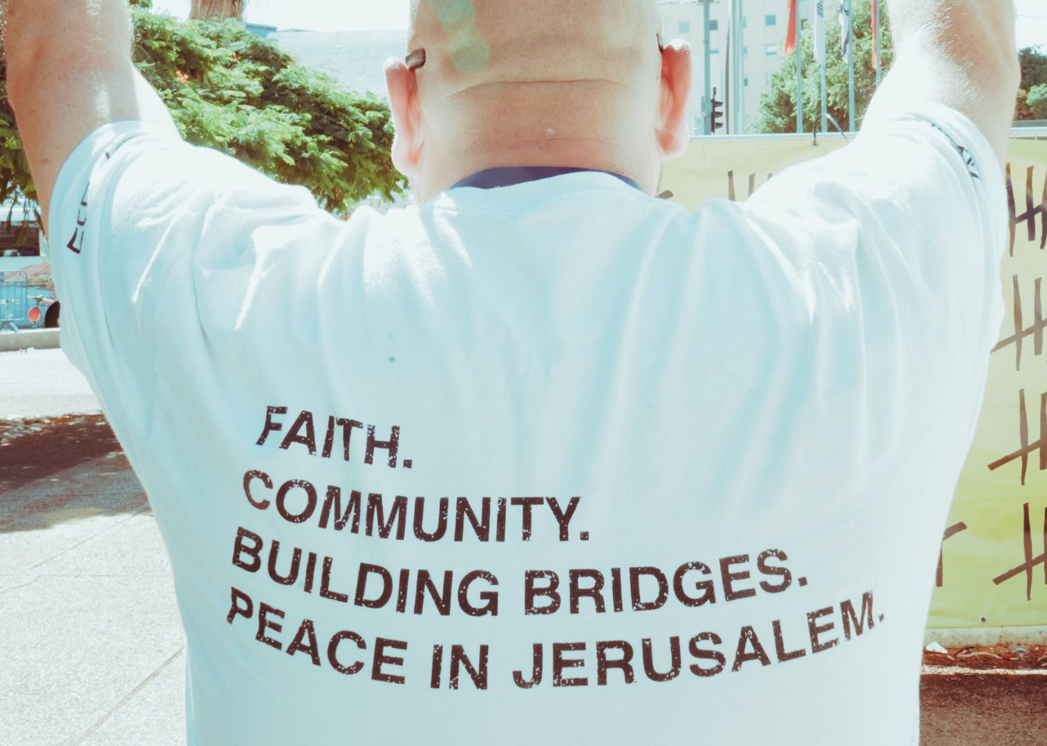Man raising hands with T-shirt that reads Faith. Community. Building Bridges. Peace in Jerusalem.